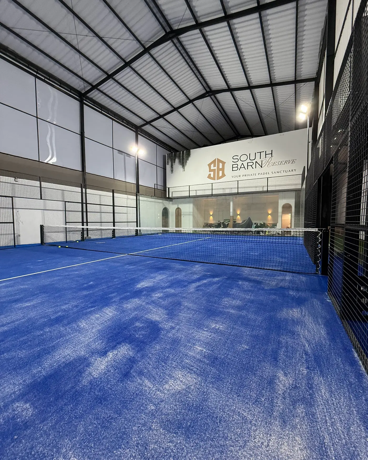 The cobalt-blue South Barn Reserve padel court under its high roof, with the Reserve sign at the far end